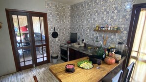 Un comedor con una mesa de madera, sillas, una cocina al fondo y papel tapiz estampado.