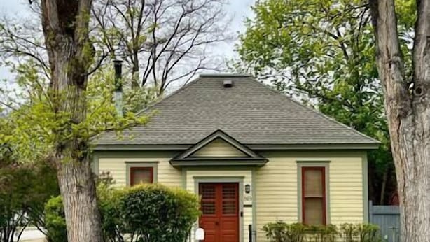 A two-story house with a red front door, a small porch, and a chimney.