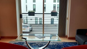 Una sala de estar moderna con una mesa de vidrio, dos sillas rojas, un tapete azul y vistas a un edificio con balcones.