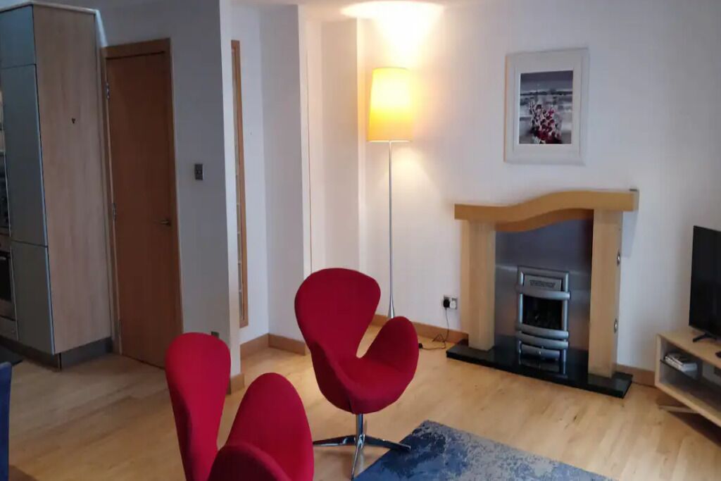 A living room with a fireplace, red chairs, a lamp, and a TV.