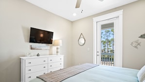 Un dormitorio con cama, televisor montado en la pared, cómoda y puerta que da a un espacio exterior.