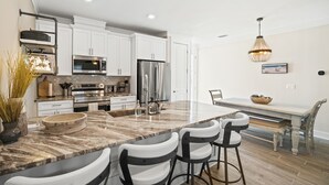 Una cocina moderna con armarios blancos, electrodomésticos de acero inoxidable y una isla de mármol con taburetes.