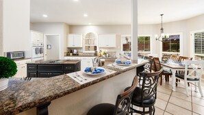 Una cucina moderna con piani in granito, mobili bianchi e un'area pranzo con un'isola grande e sgabelli da bar.