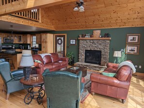 Ein großzügiges Wohnzimmer mit Ledersofas, einem Kamin aus Stein und Holzbalken an der Decke.