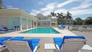 Un espace piscine avec des chaises longues bleues, une piscine à eau claire et un bâtiment à la façade blanche.