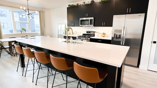 Una cocina moderna con una isla central, armarios negros, electrodomésticos de acero inoxidable y un comedor con sillas.