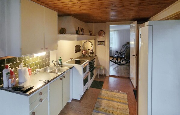 Una cocina compacta con armarios blancos, techo de madera y un taburete pequeño.