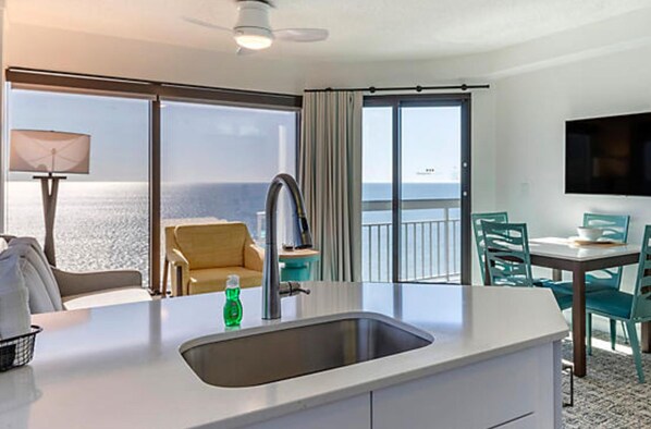 A hotel room with a balcony, a sink, a chair, a table, and a TV.