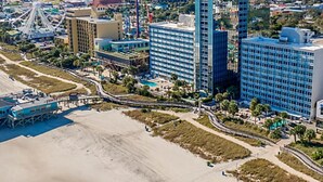 A coastal cityscape with a large Ferris wheel, modern high-rise buildings, and a beachfront promenade. - SEAGLASS TOWER MYRTLE BEACH 6 NIGHTS Sept 28-Oct 4,2026 DELUXE OCEANFRONT 1 BDRM (Myrtle Beach)