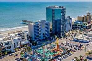A coastal cityscape with a prominent high-rise building, a beach, and a theme park. - SEAGLASS TOWER MYRTLE BEACH 7 NIGHTS MAR.10-17,2024 DELUXE -OCEANFRONT ONE BDRM (Myrtle Beach)