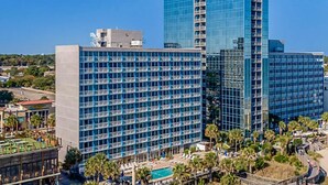 A modern hotel with a glass facade, multiple floors, and a pool area with palm trees. - SEAGLASS TOWER MYRTLE BEACH 6 NIGHTS Sept 28-Oct 4,2026 DELUXE OCEANFRONT 1 BDRM (Myrtle Beach)