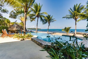 A pool area with lounge chairs and palm trees, overlooking the ocean.