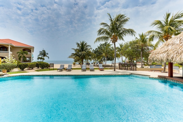 A clear blue pool with lounge chairs, palm trees, and a building with a red roof.