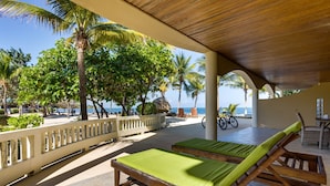 A covered outdoor seating area with wooden loungers and a view of the ocean. - Beachfront 2BR Villa with Pool & Spacious Layout (Placencia)