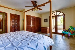 A bedroom with a bed, wooden wardrobe, a ceiling fan, and a view of the outside.