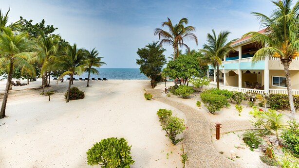 Un resort sulla spiaggia, con spiaggia sabbiosa, palme e un edificio con balcone vista mare.