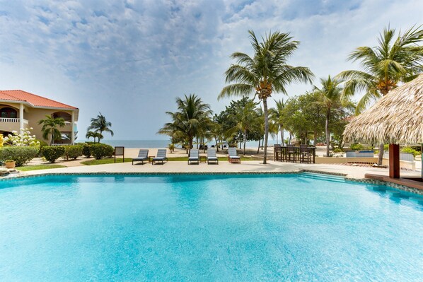 A swimming pool with lounge chairs, palm trees, and a building with a red roof.