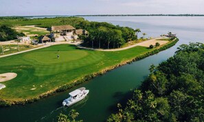 A golf course with a waterway, a boat, and a building with a thatched roof.