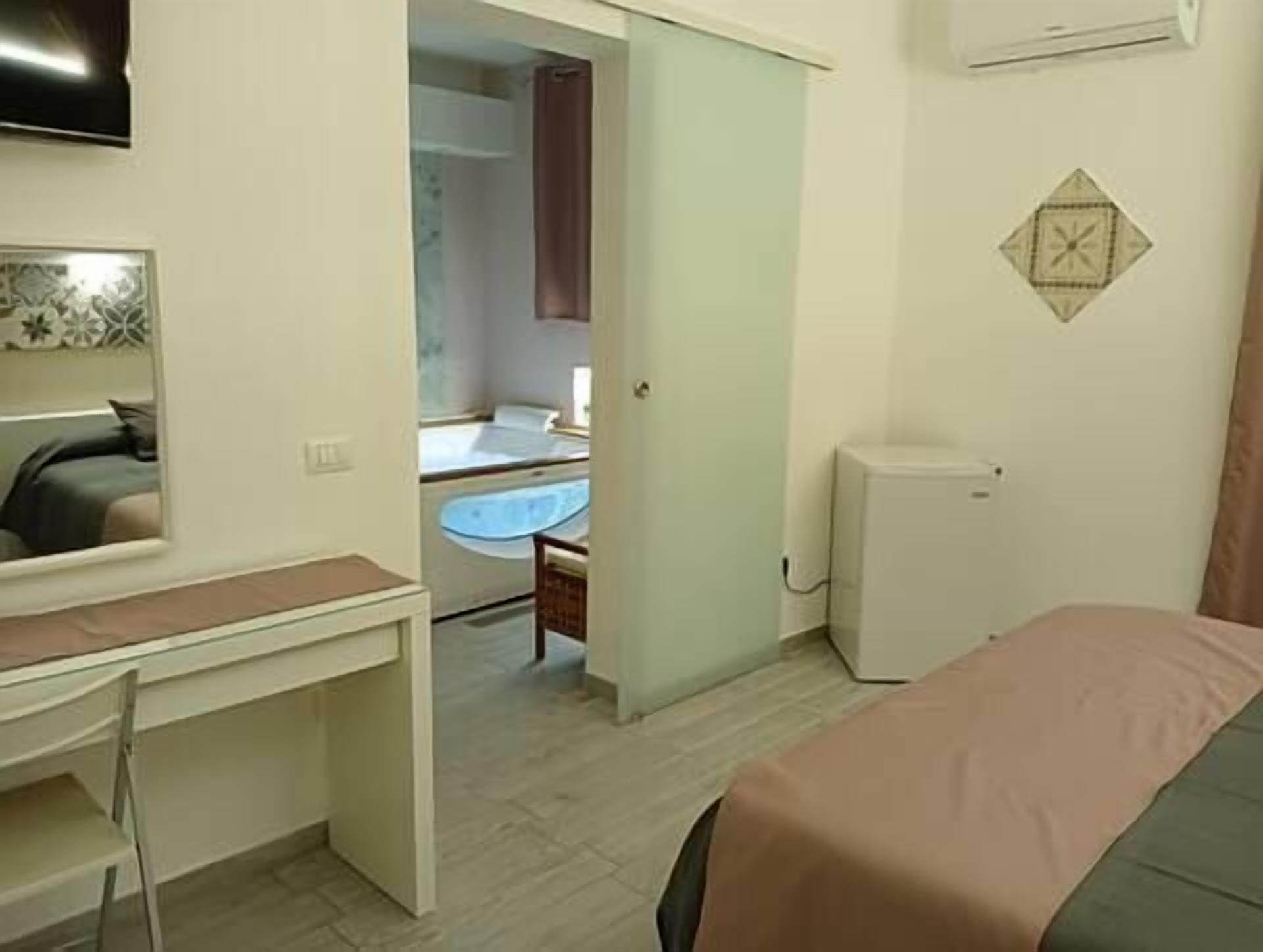 A hotel room with a bed, a desk, a chair, a TV, a bathroom with a sink, and a shower.