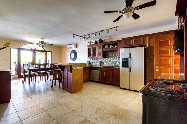 A spacious kitchen with a central island, dark wooden cabinets, stainless steel appliances, and a ceiling fan.