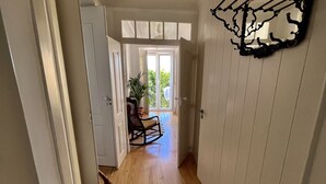 Ein Flur mit Holzboden, weißen Wänden und einem Deckenventilator. Links befindet sich eine Tür und in der Mitte ein Zimmerpflanze.