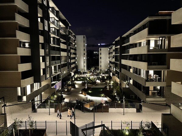 A modern apartment complex with multiple balconies, a central courtyard with plants, and a nighttime view.