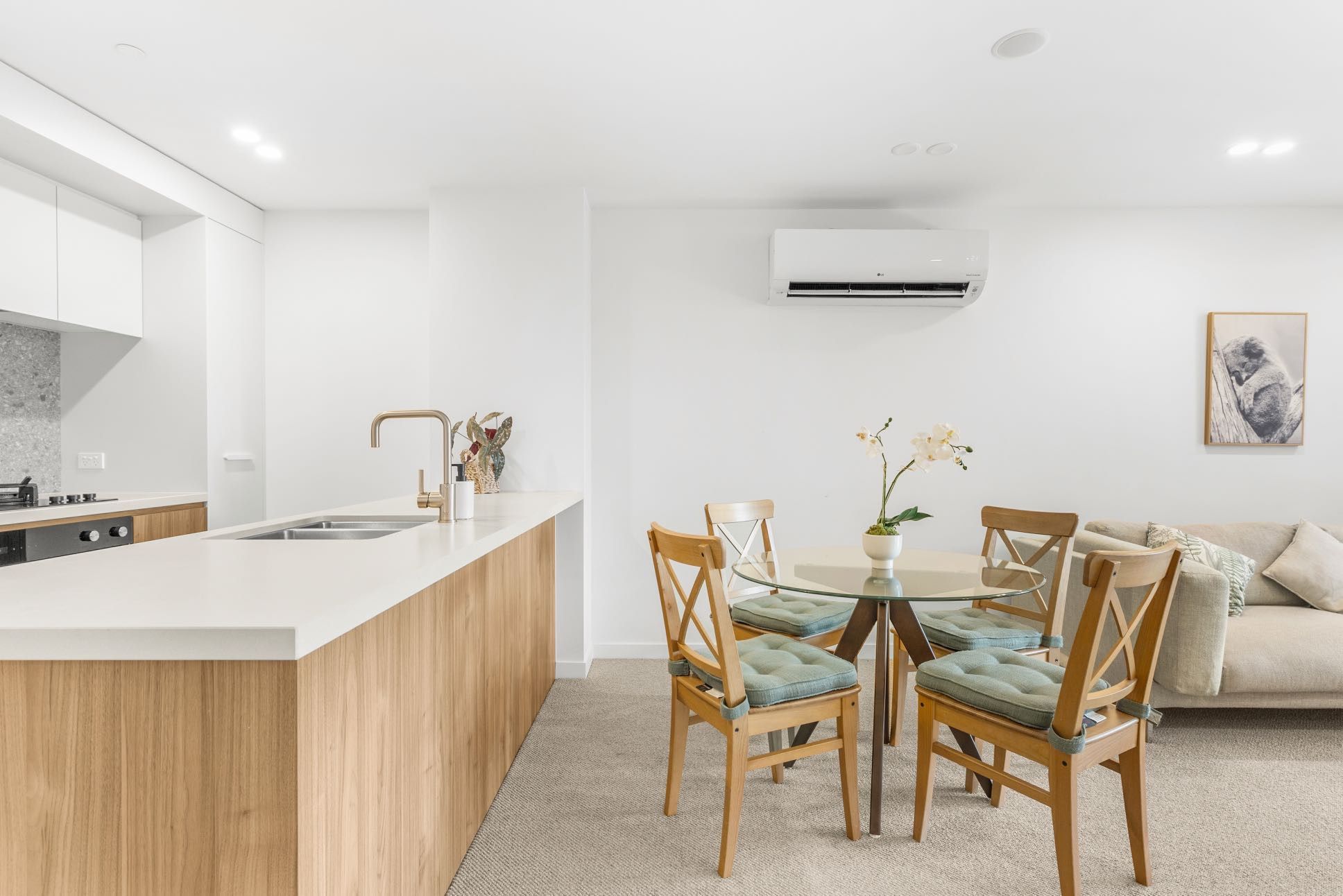 A modern kitchen with a central island, a dining area with four chairs, and a living space with a sofa and a framed picture.