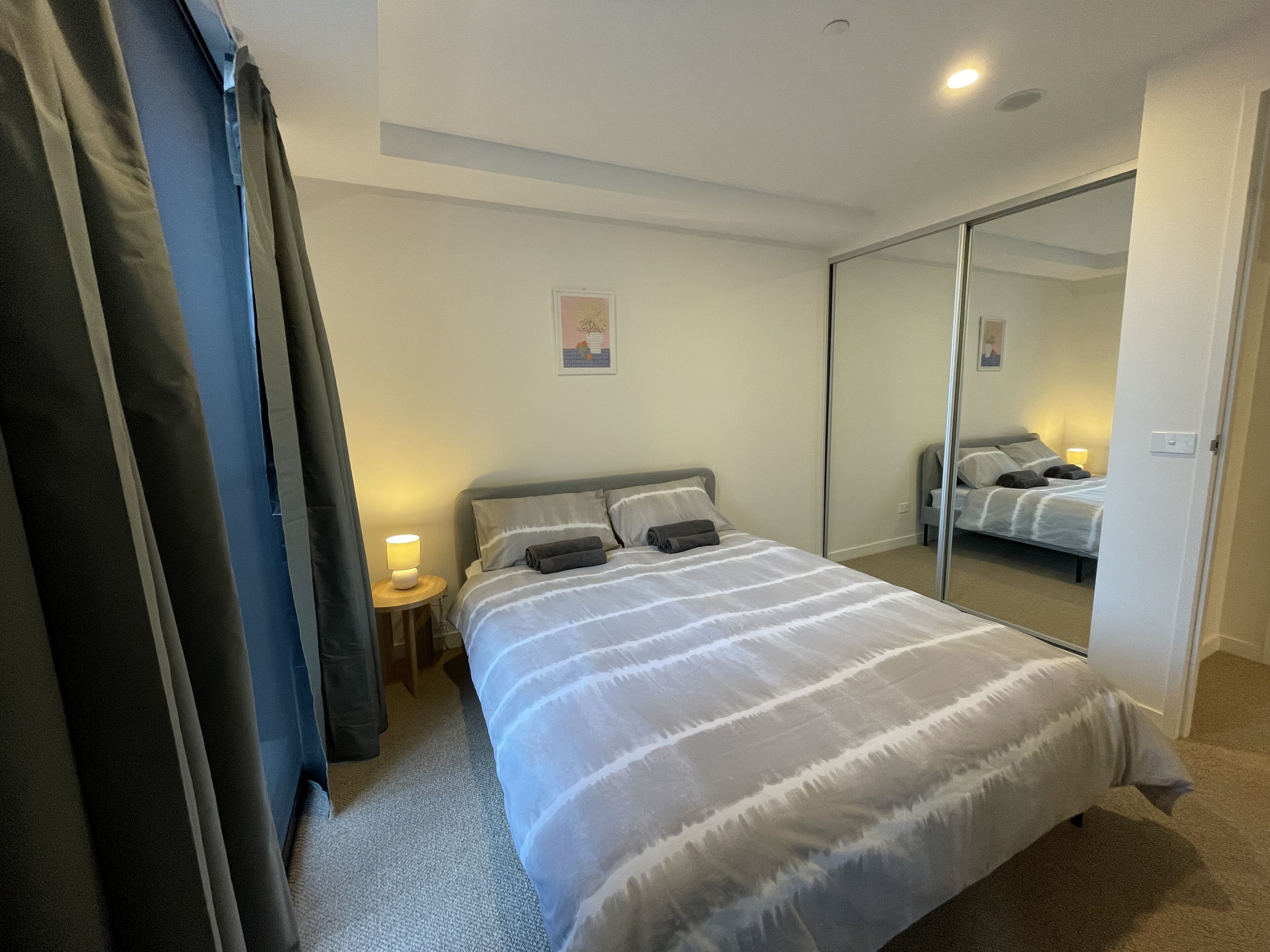 A bedroom with a bed, a nightstand, a mirror, and a door.