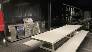 An outdoor patio with a stainless steel grill and a white table with benches.