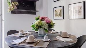 A dining area with a round table, black chairs, a vase of flowers, and framed pictures on the wall.