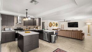 Una cocina moderna con armarios oscuros, una isla central y un comedor con sofá y televisor.