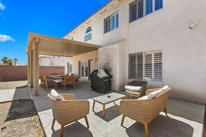Une terrasse extérieure aménagée avec des meubles en osier, un barbecue et un espace salon abrité.