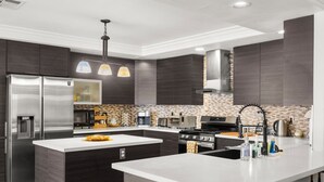 Una cocina moderna con armarios oscuros, electrodomésticos de acero inoxidable, una isla central e iluminación colgante.