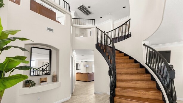 Un interior espacioso con una escalera curva, un balcón en el segundo piso y una sala de estar con sofá.