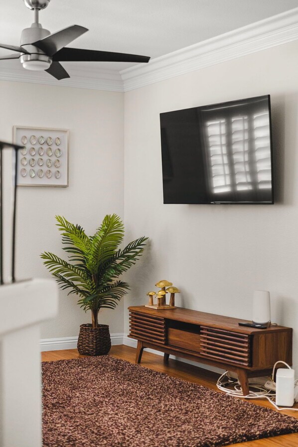 A room with a ceiling fan, a flat-screen TV mounted on the wall, a wooden sideboard, a potted plant, and a patterned rug.