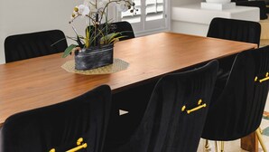 Un comedor con una mesa de madera, sillas negras con detalles dorados, una araña y contraventanas blancas.