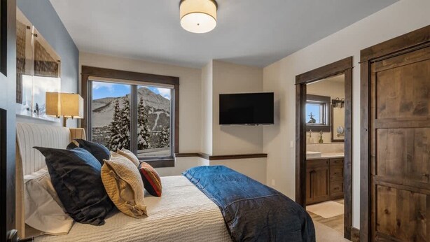 A bedroom with a bed, a window with a mountain view, a television, and a wooden door. - Ski-In/Ski-Out Updated Big Sky Retreat (Big Sky)