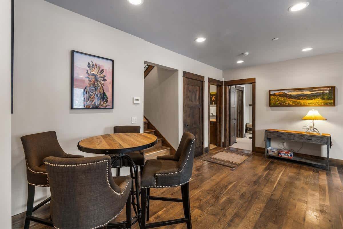 A dining area with a round wooden table and upholstered chairs, a staircase leading to another room, and a painting on the wall.