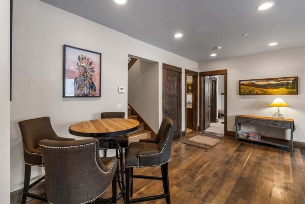 Un comedor con una mesa redonda de madera y sillas tapizadas, una escalera que conduce a otra habitación, y un cuadro en la pared.