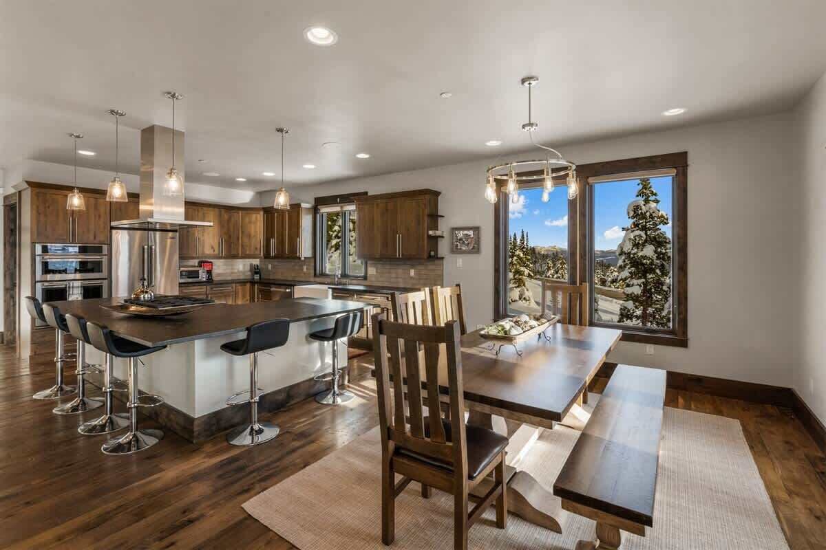 A modern kitchen with a central island, bar stools, and a dining table with benches.