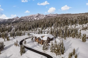 A lodge in a snowy forest with a clear road leading to it. - Ski-In/Ski-Out Updated Big Sky Retreat (Big Sky)