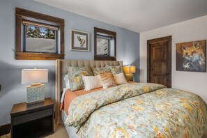 A bedroom with a large bed, two bedside tables, a window with a view, and a door. - Ski-In/Ski-Out Updated Big Sky Retreat (Big Sky)