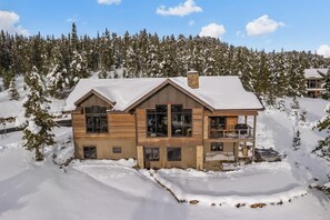A two-story log cabin with a balcony, surrounded by snow-covered trees. - Ski-In/Ski-Out Updated Big Sky Retreat (Big Sky)