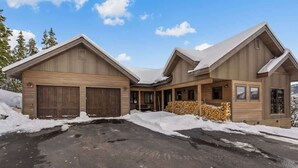 A two-story wooden cabin with a garage, a covered porch, and a snow-covered driveway. - Ski-In/Ski-Out Updated Big Sky Retreat (Big Sky)