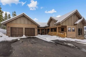 A two-story wooden cabin with a garage, a covered porch, and a snow-covered driveway. - Ski-In/Ski-Out Updated Big Sky Retreat (Big Sky)