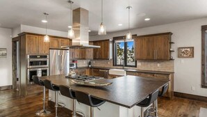 A modern kitchen with wooden cabinets, stainless steel appliances, and a central island with bar stools. - Ski-In/Ski-Out Updated Big Sky Retreat (Big Sky)