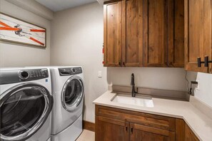 A laundry room with a washing machine, a sink, wooden cabinets, and a wall-mounted artwork.