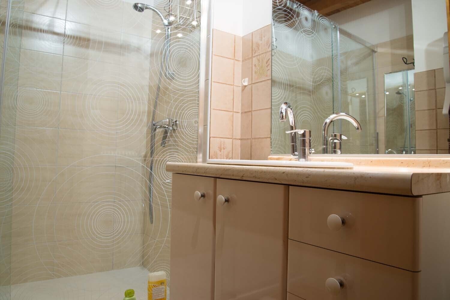 Un bagno con box doccia in vetro, lavabo con specchio e mobili beige.
