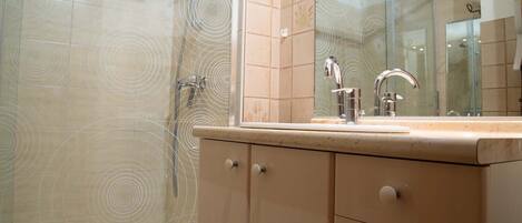 Un bagno con box doccia in vetro, lavabo con specchio e mobili beige.