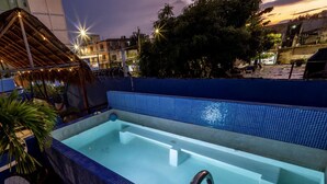 Ein Dachpool mit blau gefliestem Rand, umgeben von Kübelpflanzen und einer Reetdachkonstruktion.